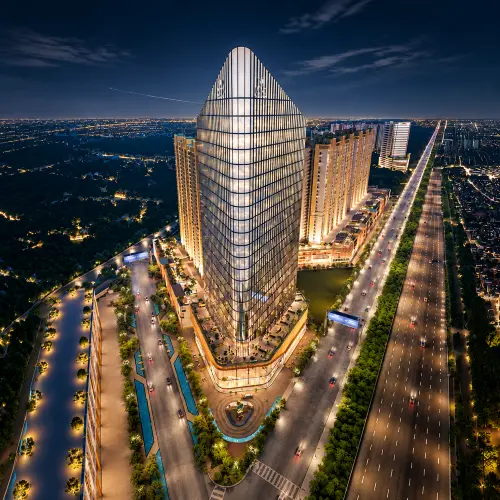 M3M CFC commercial tower in Gurgaon at night, illuminated against the city skyline with landscaped surroundings, connected roads, and nearby high-rise buildings.